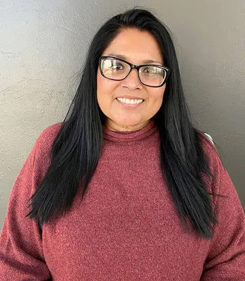 A female staff member wearing glasses and a pink sweater is smiling at the camera.