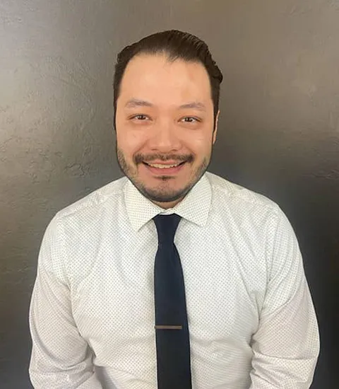 A male staff member wearing a white shirt and a black tie is smiling at the camera.