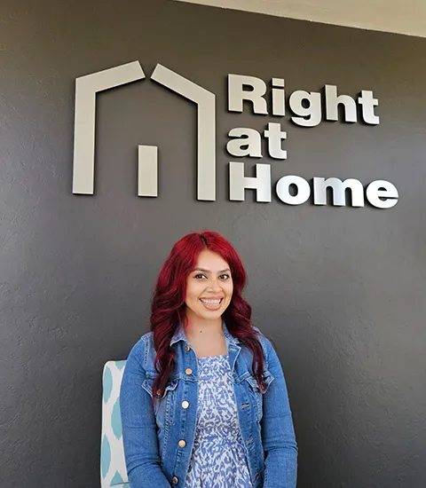 A woman with red hair in a denim jacket poses in front of the company logo.