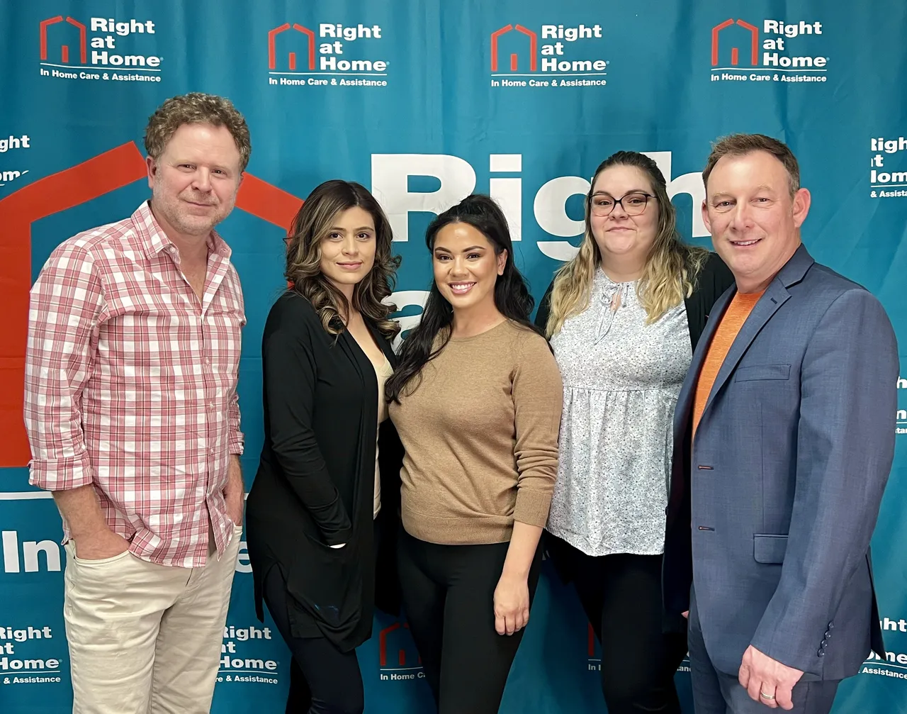 Official group photo of five employees posing in front of the Right at Home In Home Care & Assistance brand backdrop.