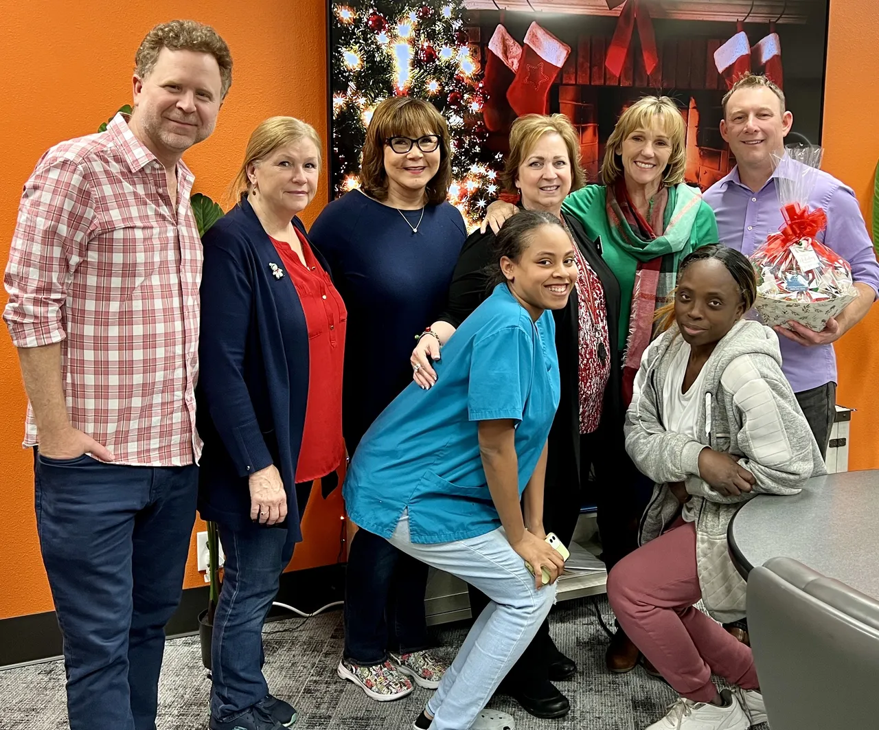 Team photo of nine employees posing together in front of an orange background with Christmas decorations.