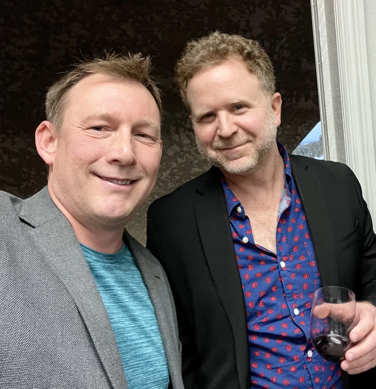 Two men pose together indoors, smiling.