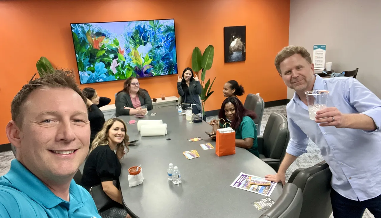 Employees meet in an office with orange walls and a black conference table.